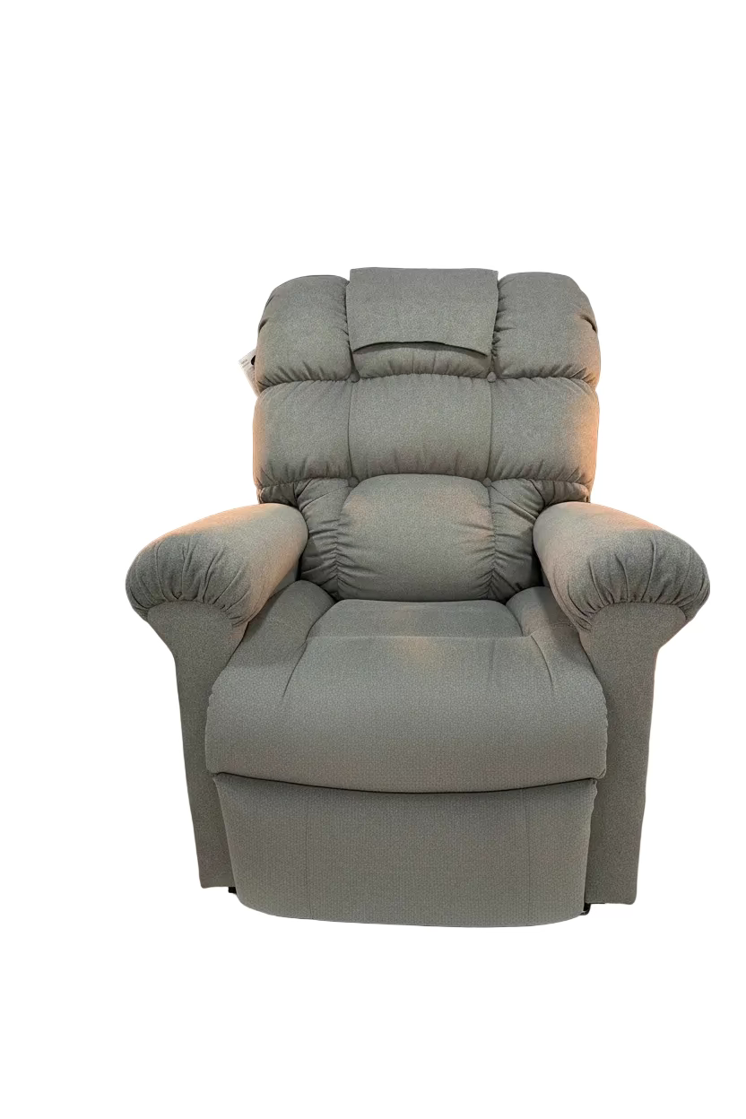 A gray upholstered recliner chair displayed indoors on a white pedestal in front of a dark blue wall with a large 'MUST MEDICAL' logo. The chair is wrapped in clear plastic on the seat and back, with a product tag attached.