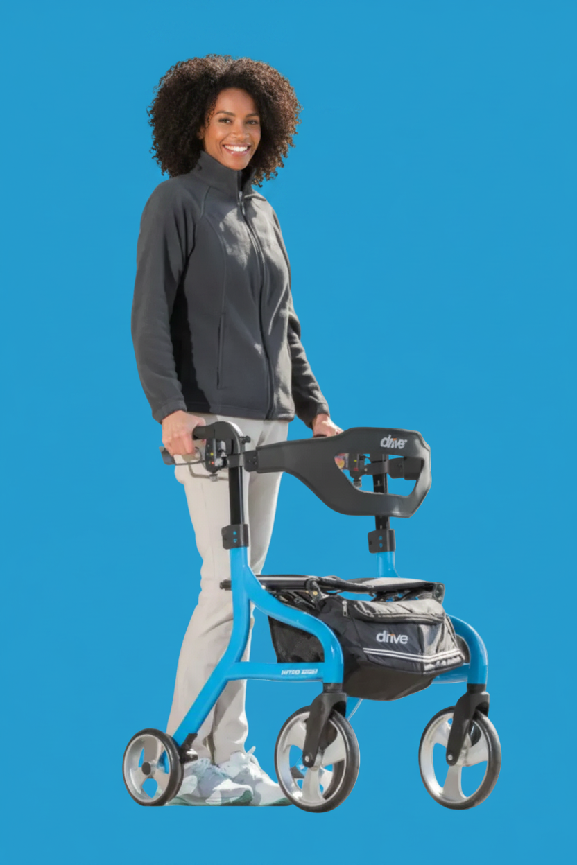 A woman wearing a dark gray zip-up jacket and light gray pants stands next to a blue and black Drive mobility walker against a solid blue background.