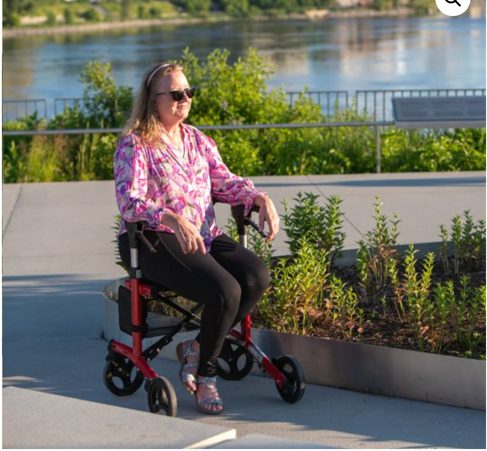 Person using a mobility scooter by a waterfront with greenery in the background