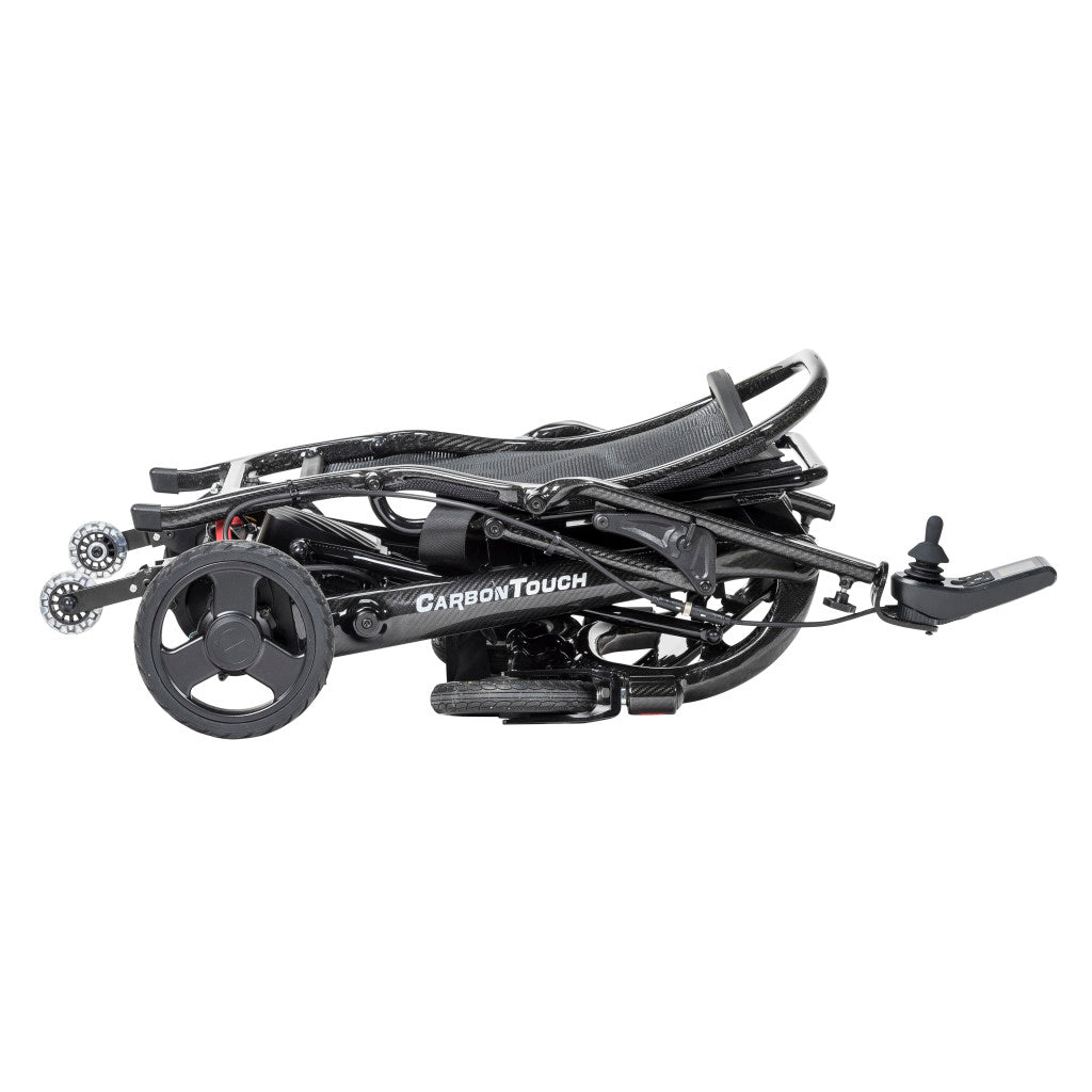 Drive Carbon Touch electric wheelchair in fully folded position showing compact flat profile with rear drive wheel, front casters, joystick controller, push handle, and carbon fiber frame — available at Must in Metro Vancouver