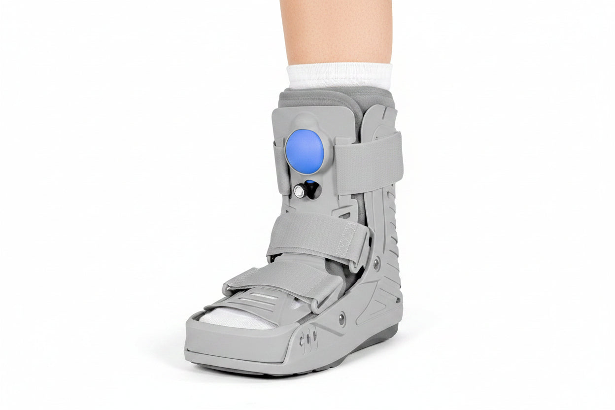 Grey pneumatic air CAM walking boot with blue air pump bladder, rigid shell, and velcro straps worn on foot with white sock — side view showing structured ankle and foot immobilization boot for fracture recovery