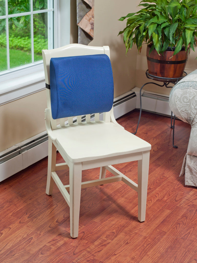 Blue lumbar support cushion strapped to white wooden chair in a home living room setting, showing everyday back support use
