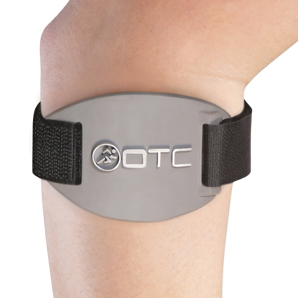OTC 2421 tennis elbow brace worn on forearm below elbow showing grey oval pressure pad with OTC logo, black elastic strap, and velcro closures on white background
