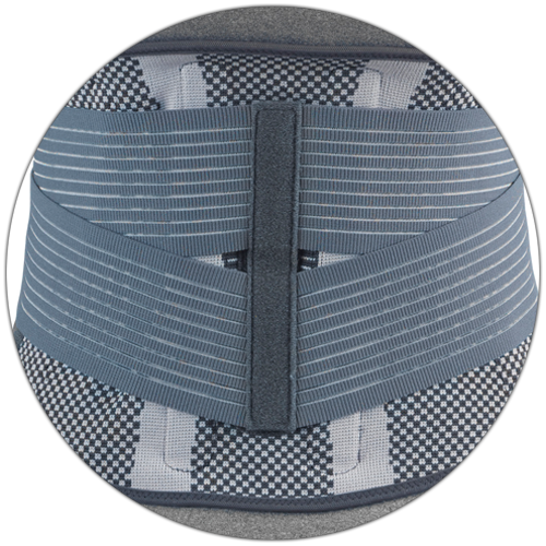 Close-up circle crop of OTC 2882 Theratex lumbosacral support centre showing vertical rigid stay with buckle hardware, diagonal ribbed elastic tension bands, and knit mesh border panels
