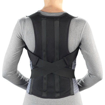 OTC Comfort Posture Brace with Rigid Stays in black – rear view worn by a person in a grey long-sleeve shirt, showing breathable mesh back panel, vertical rigid stays, criss-cross lumbar straps, and lower back support band on white background