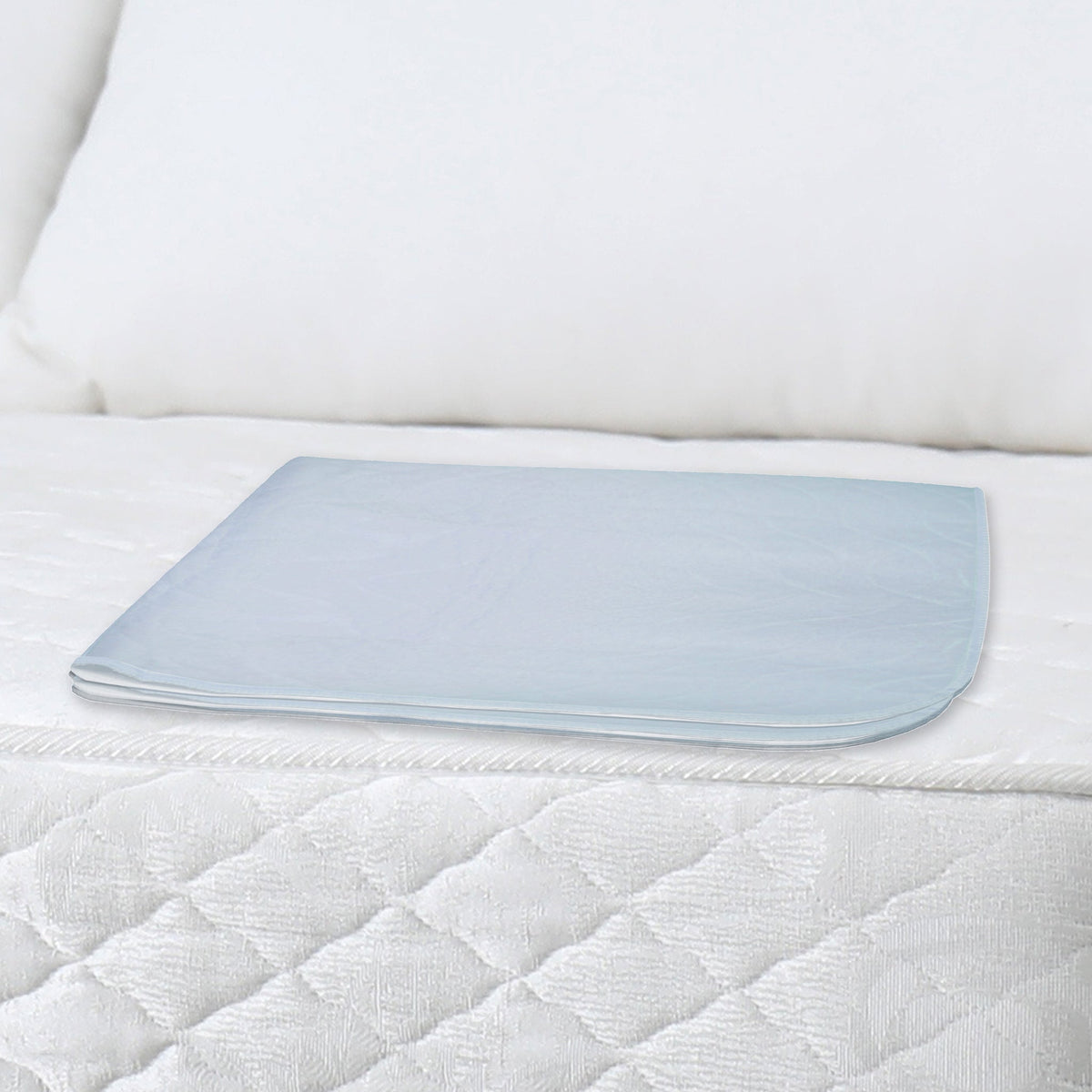 PCP 6254 reusable washable bed pad folded and placed on a white quilted mattress with pillow in background – light blue waterproof side visible – Must
