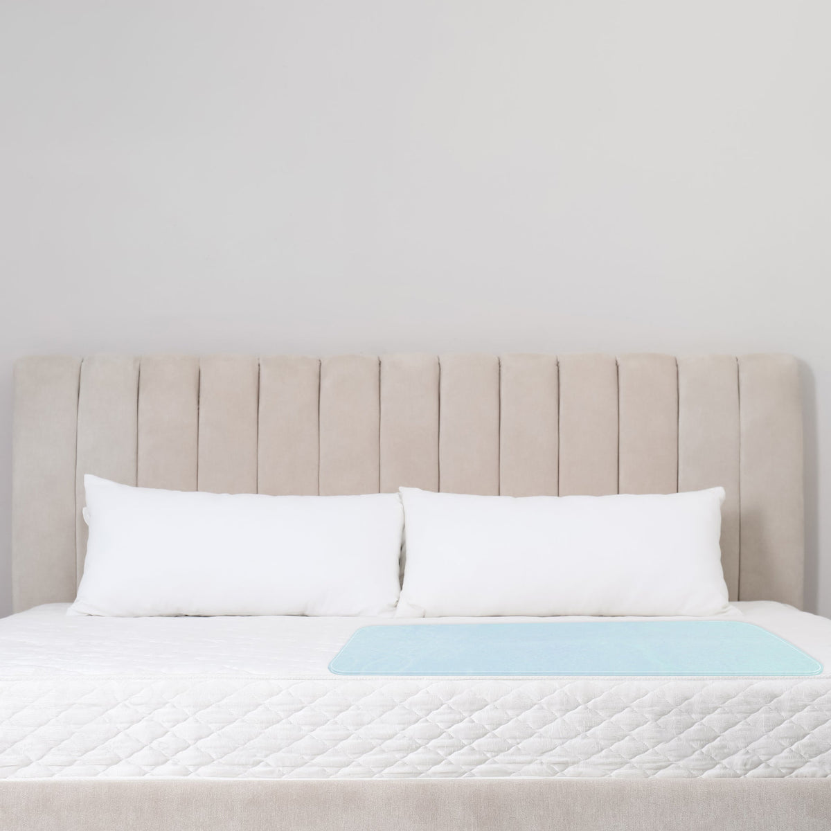 PCP 6254 reusable washable bed pad placed on a white bed with two pillows and beige upholstered headboard – light blue waterproof side visible – Must