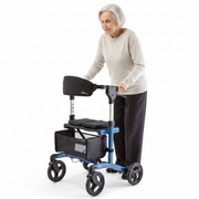 An elderly woman with short gray hair is shown using a blue and black rolling walker with a seat, armrests, and a storage basket, set against a plain white studio background.
